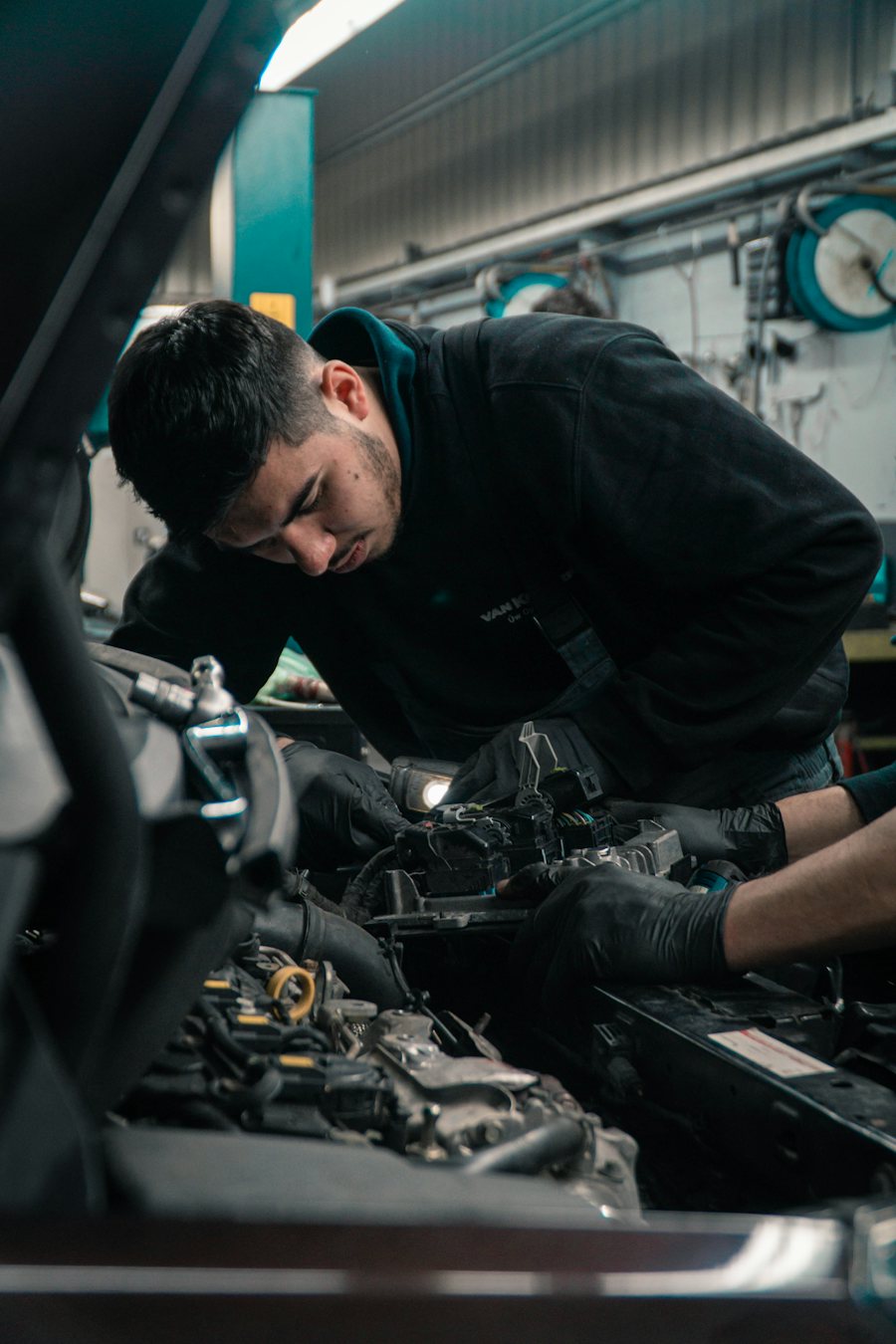 Mobile mechanic working on a car engine under an open bonnet with a work light